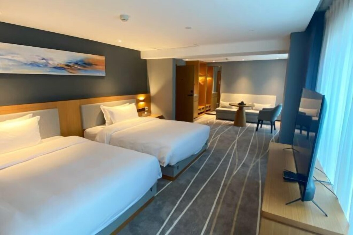 A hotel room with two beds, a desk, a chair, and a TV.