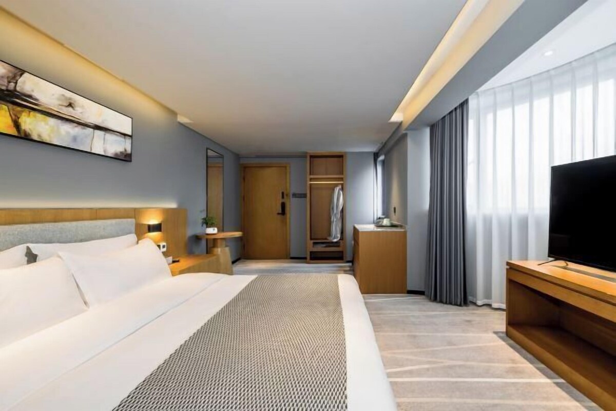 A modern hotel room with a large bed, a television, a wardrobe, and a bathroom visible through an open door.