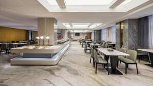 A modern hotel dining area with a central bar, multiple tables, and a high ceiling with skylights. - Chenggong Hotel (Xiamen Gaoqi Airport SM Plaza) (Xiamen)