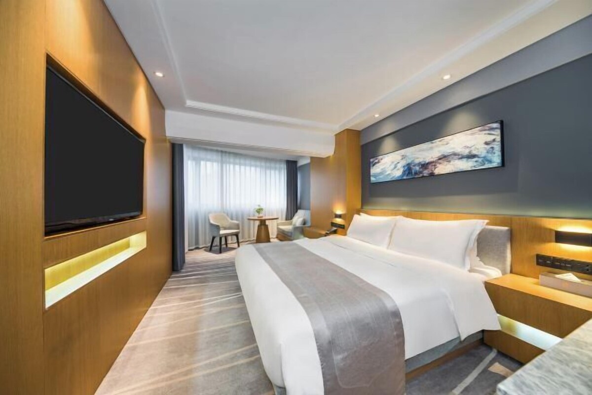 A modern hotel room with a large bed, a flat-screen TV, a desk, and a chair.