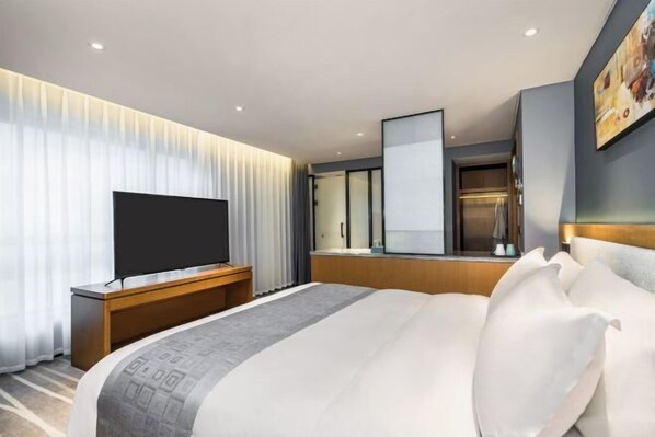 Moderni hotellihuone, jossa on suuri sänky, taulutelevisio, puinen konsolipöytä ja suuri peili.