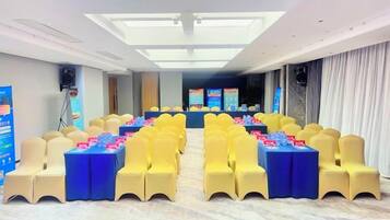 A conference room with rows of yellow chairs, a stage with a podium, and a large screen.