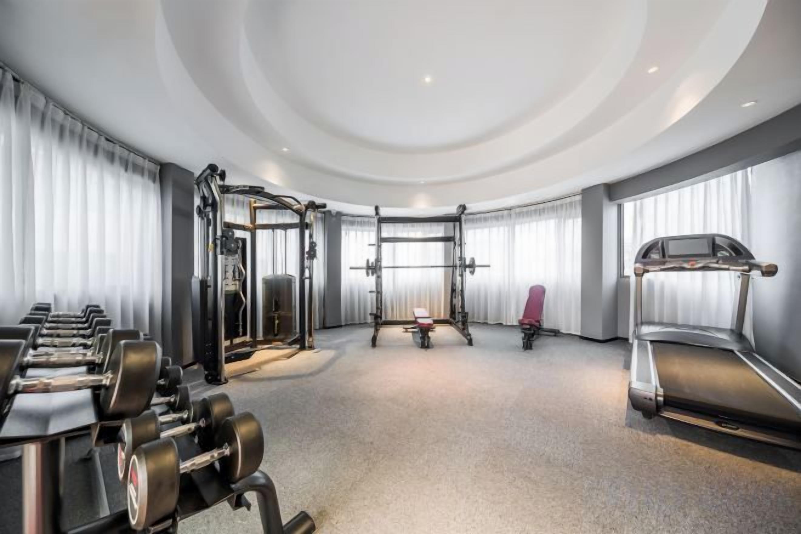 A gym with exercise equipment, including dumbbells, a squat rack, and a treadmill.
