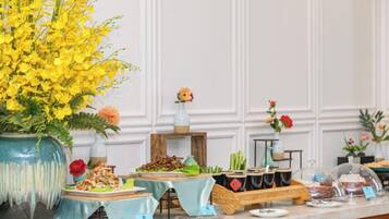A buffet setup with various dishes and a large vase of yellow flowers.