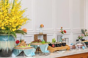 A buffet setup with various dishes and a large vase of yellow flowers.
