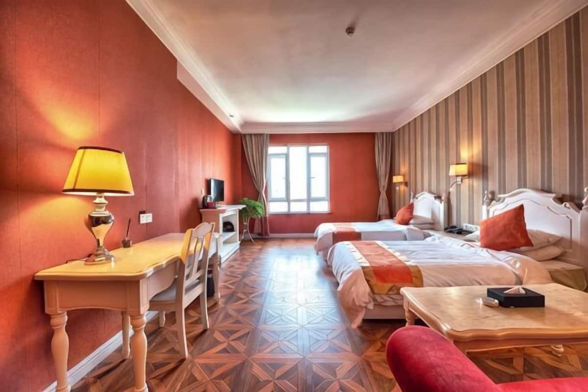 A hotel room with two beds, a desk, a chair, a lamp, and a TV.