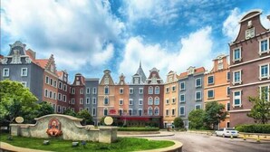 A row of multi-story buildings with a central courtyard, featuring a statue and a sign with Chinese characters. - Xuzhou Amusement Land Resort Hotel (Xuzhou)