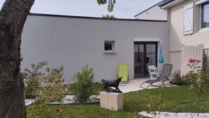 Una casa moderna con fachada gris, un patio con mobiliario exterior y un jardín con una estatua.