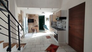 Un pasillo estrecho con una escalera a la izquierda, un comedor con mesa y sillas en el centro, y una cocina con armarios y una estufa a la derecha.
