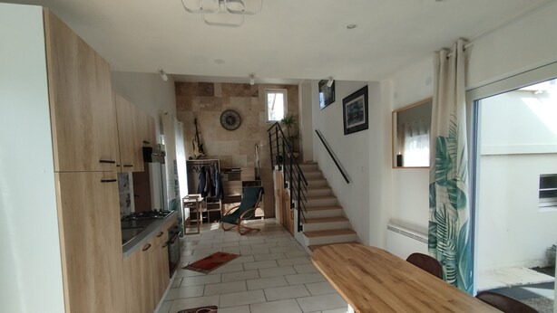 Una cocina moderna con armarios de madera, un comedor con mesa de madera y una escalera que sube a otro nivel.