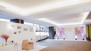 Une pièce spacieuse dotée d’un sol recouvert de moquette, d’un comptoir d’accueil blanc, d’un fauteuil rose et d’un décor floral en arrière-plan.