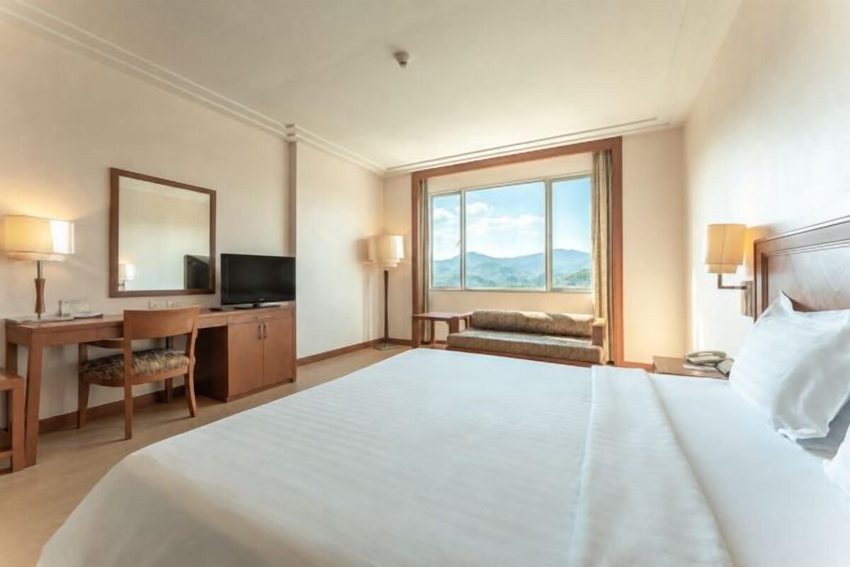 Ett hotellrum med en stor säng, ett skrivbord med en stol, en tv och ett fönster med utsikt över bergen.