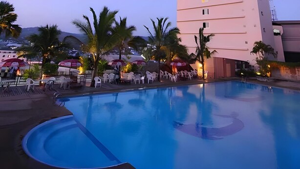 Une piscine à bords incurvés, entourée de chaises et de parasols en plastique blancs.