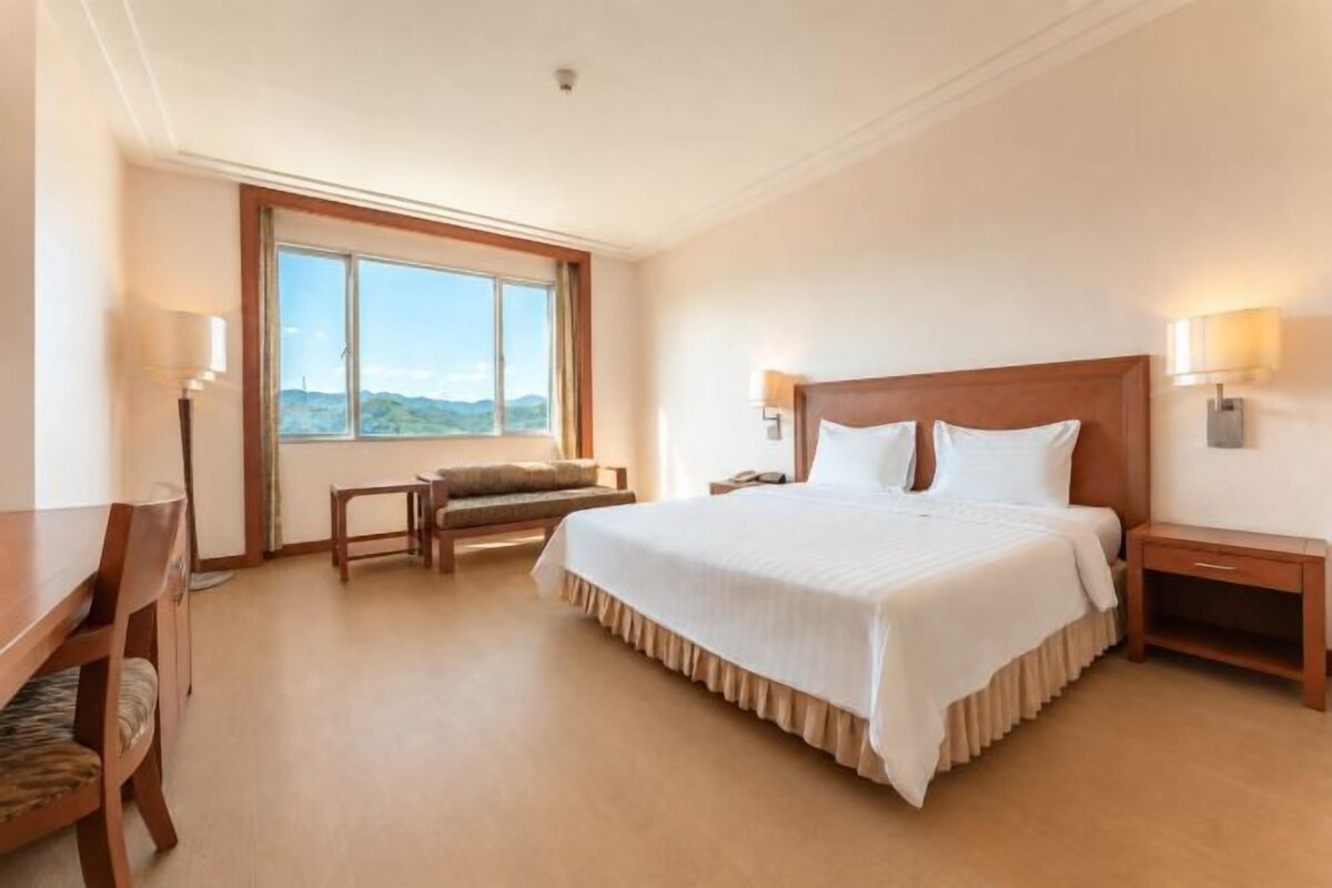 A hotel room with a large bed, bedside tables, a desk, and a chair.