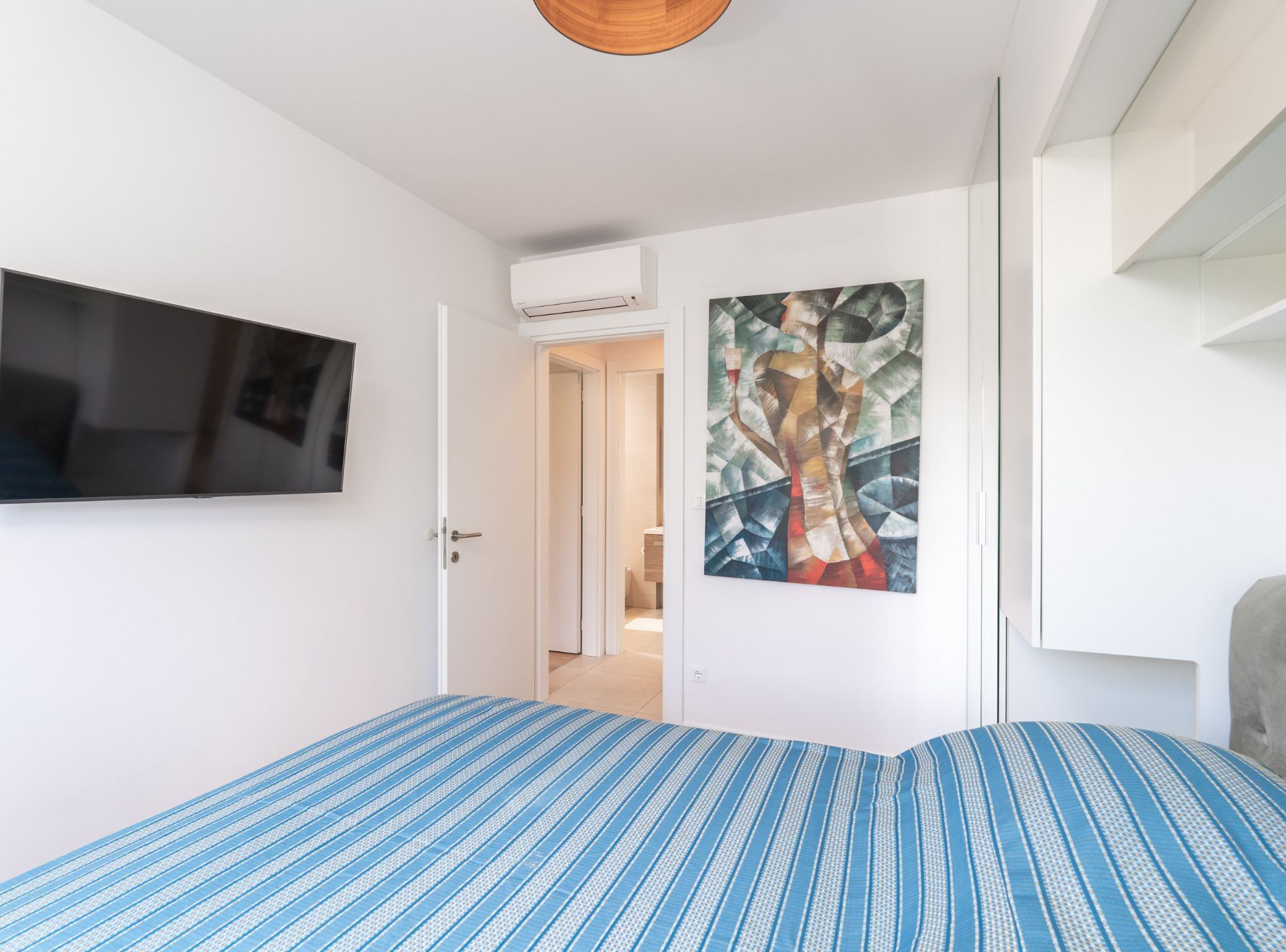 Een slaapkamer met een bed, een televisie, een airconditioner en een schilderij aan de muur.