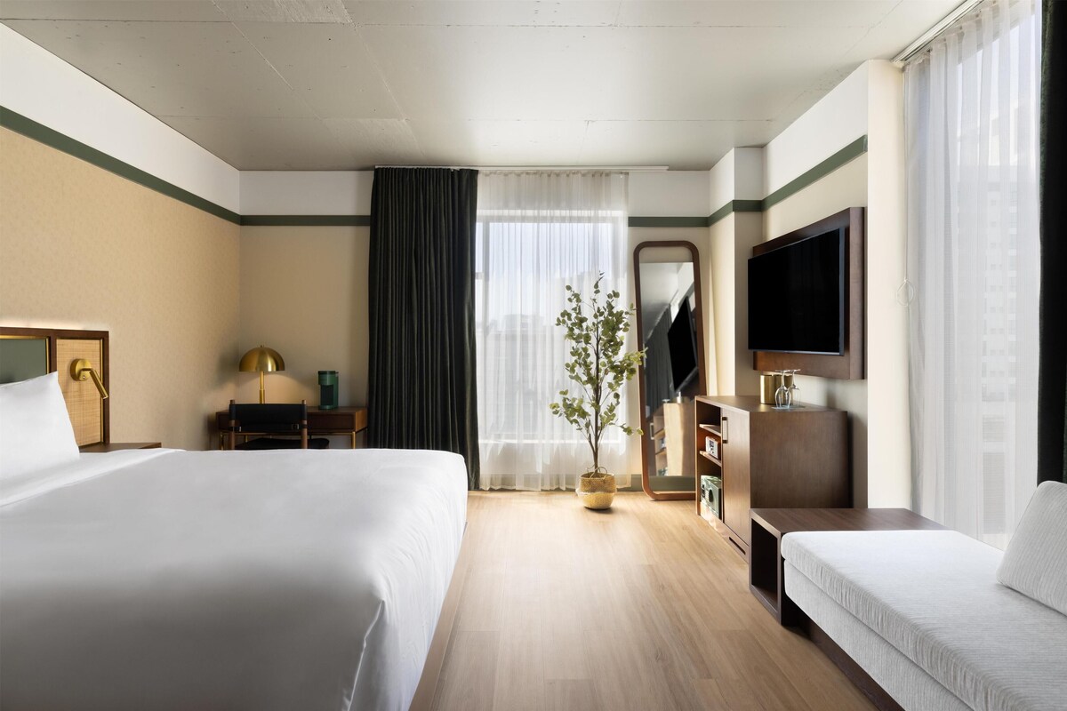 A hotel room with two beds, a TV, a desk, a lamp, a mirror, and a potted plant.