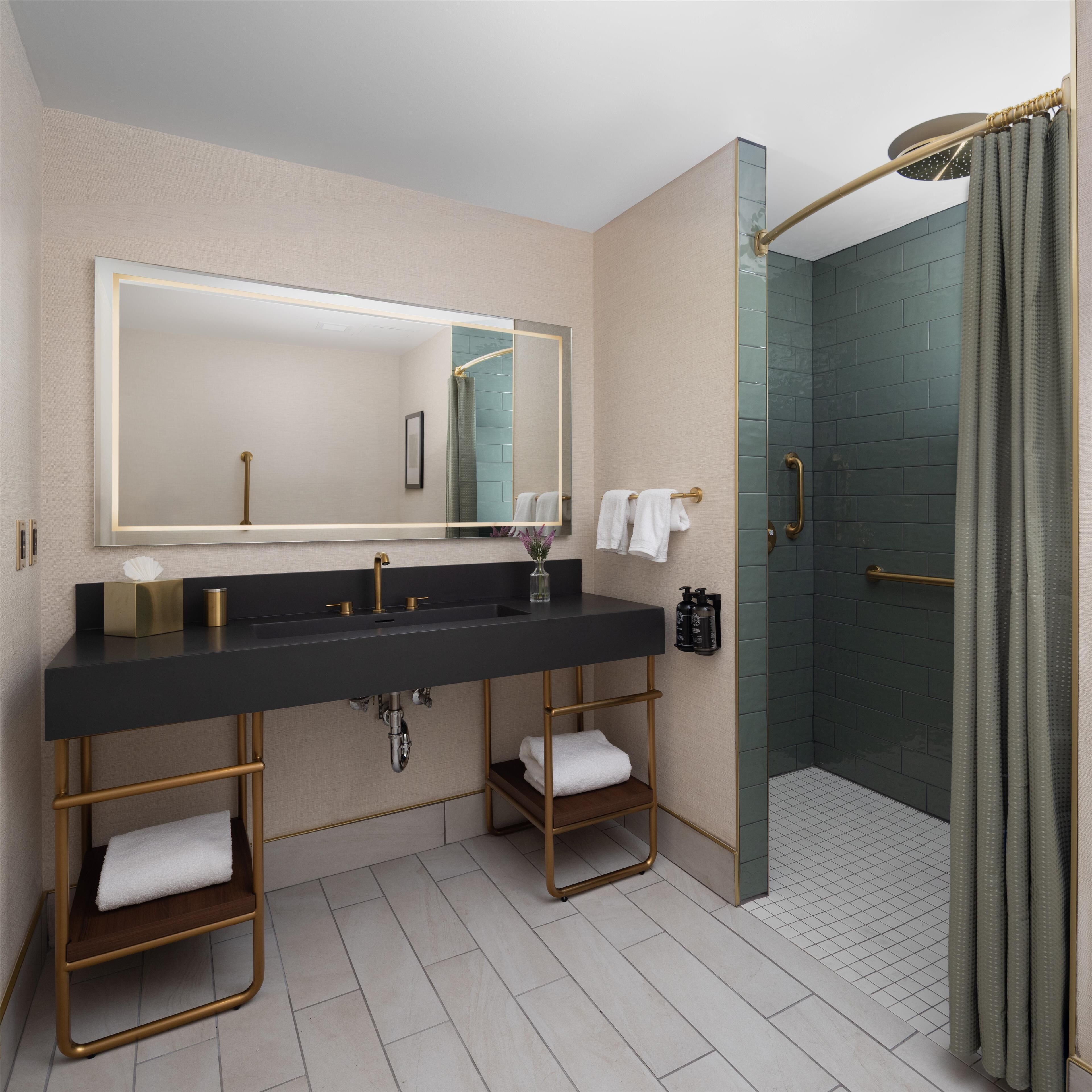 A modern bathroom with a black vanity, gold fixtures, a large mirror, and a glass-enclosed shower.
