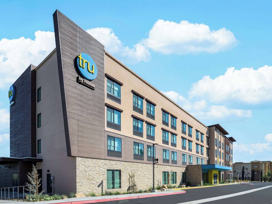 A modern hotel building with a 'TRu by Hilton' sign, multiple windows, and a parking lot.