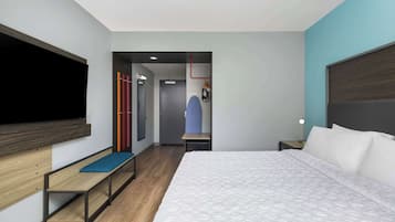 A modern hotel room with a large bed, a bench, a TV, a wardrobe, and a mirror.