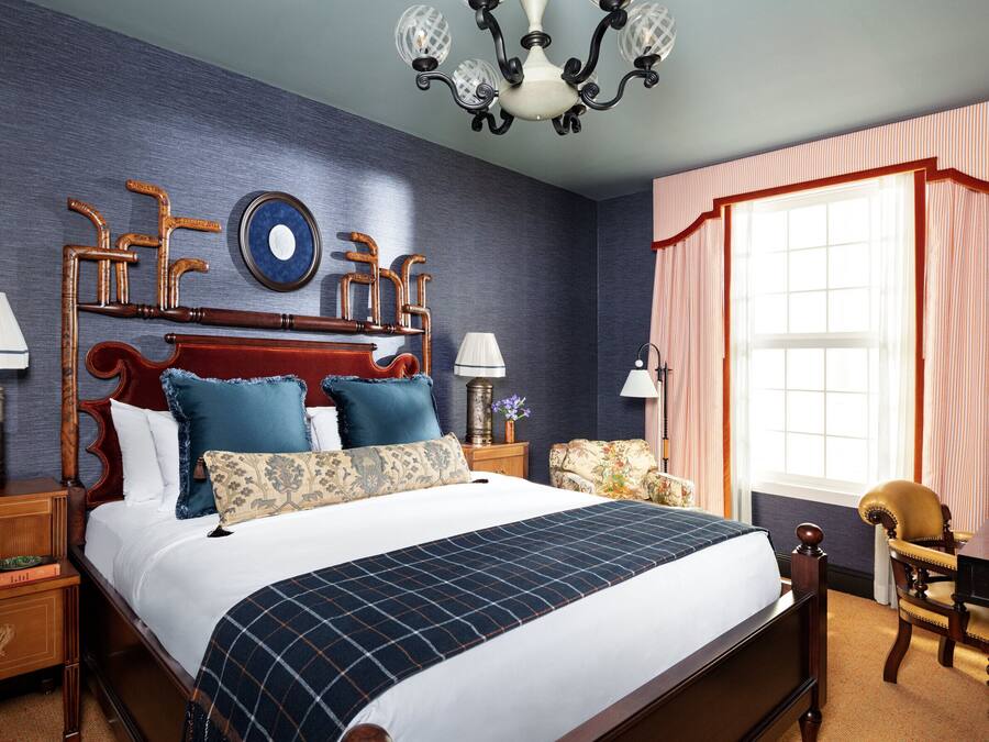 A bedroom with a large bed, wooden headboard, two nightstands, a desk, and a chair.