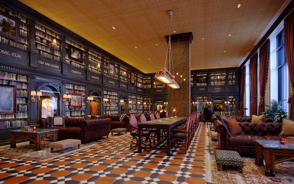Cozy library with leather sofas and armchairs, surrounded by bookshelves and a central table.