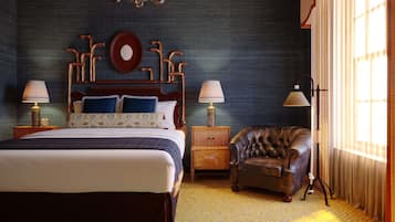 Un dormitorio con una cama grande, dos mesitas de noche, una mesita auxiliar de madera, un sillón de cuero y una lámpara de pie.