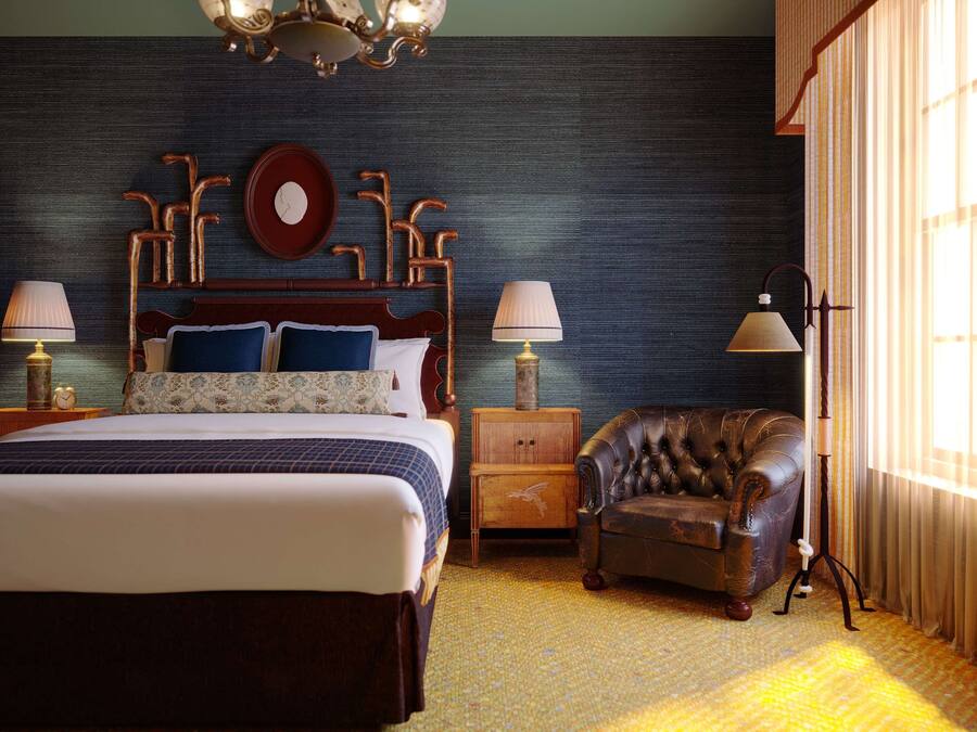 A bedroom with a large bed, two bedside tables, a wooden nightstand, a leather armchair, and a floor lamp.