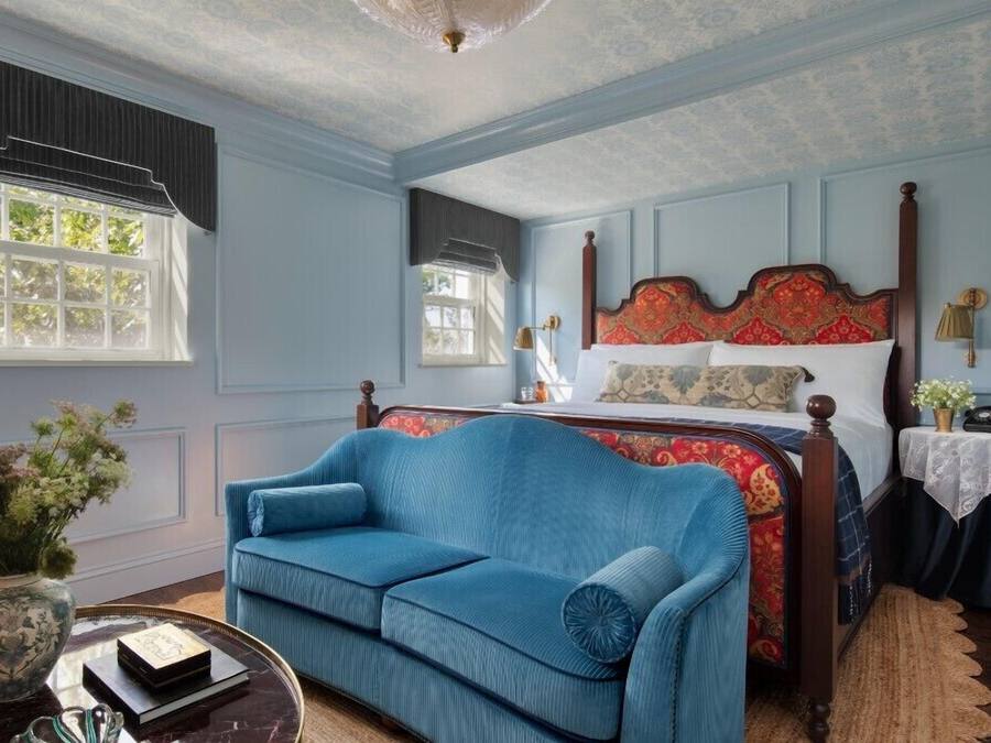 A bedroom with a large bed, a blue sofa, and a small table with a vase and books.
