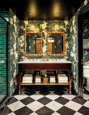 Classic bathroom with ornate mirror, wall-mounted lights, marble-topped vanity, and a forest mural.