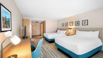 Hotellihuone, jossa on kaksi sänkyä, kirjoituspöytä lampun kanssa, tuoli ja seinällä olevia kehystettyjä kuvia.