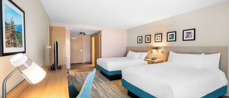 A hotel room with two beds, a desk with a lamp, a chair, and framed pictures on the wall.