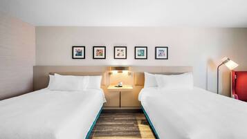 A hotel room with two beds, a nightstand, a lamp, and a wall with framed pictures.