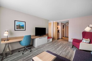 A hotel room with a desk, chair, television, and a red armchair.