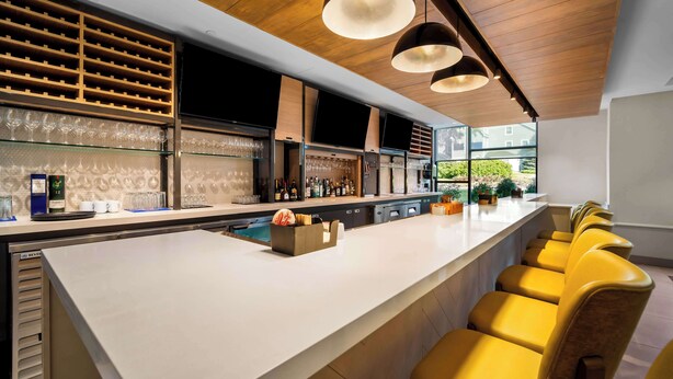 Un bar moderno con una barra larga, varias opciones de asientos y vistas al exterior.