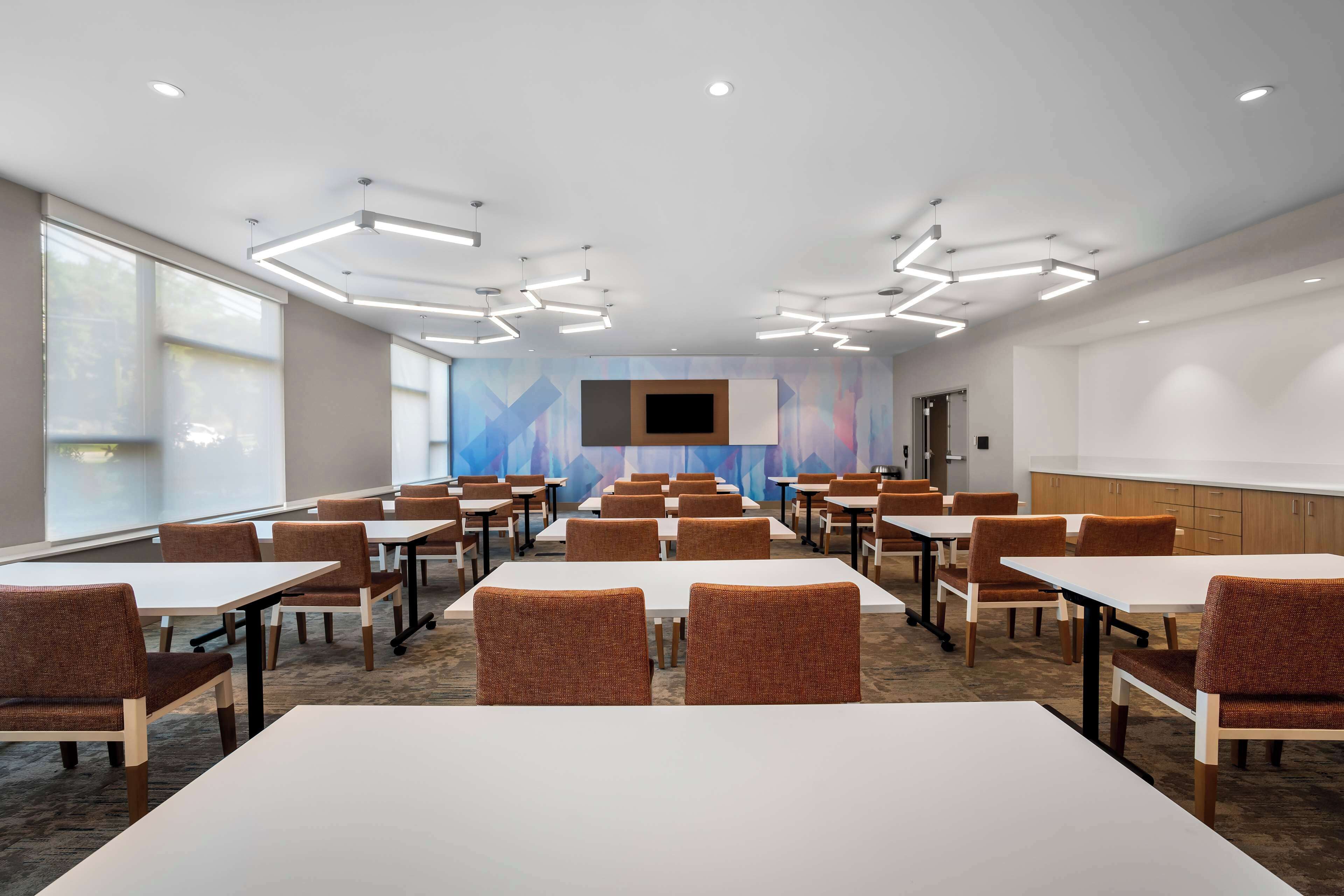 A conference room with white tables and brown chairs, a large screen, and a colorful abstract wall.
