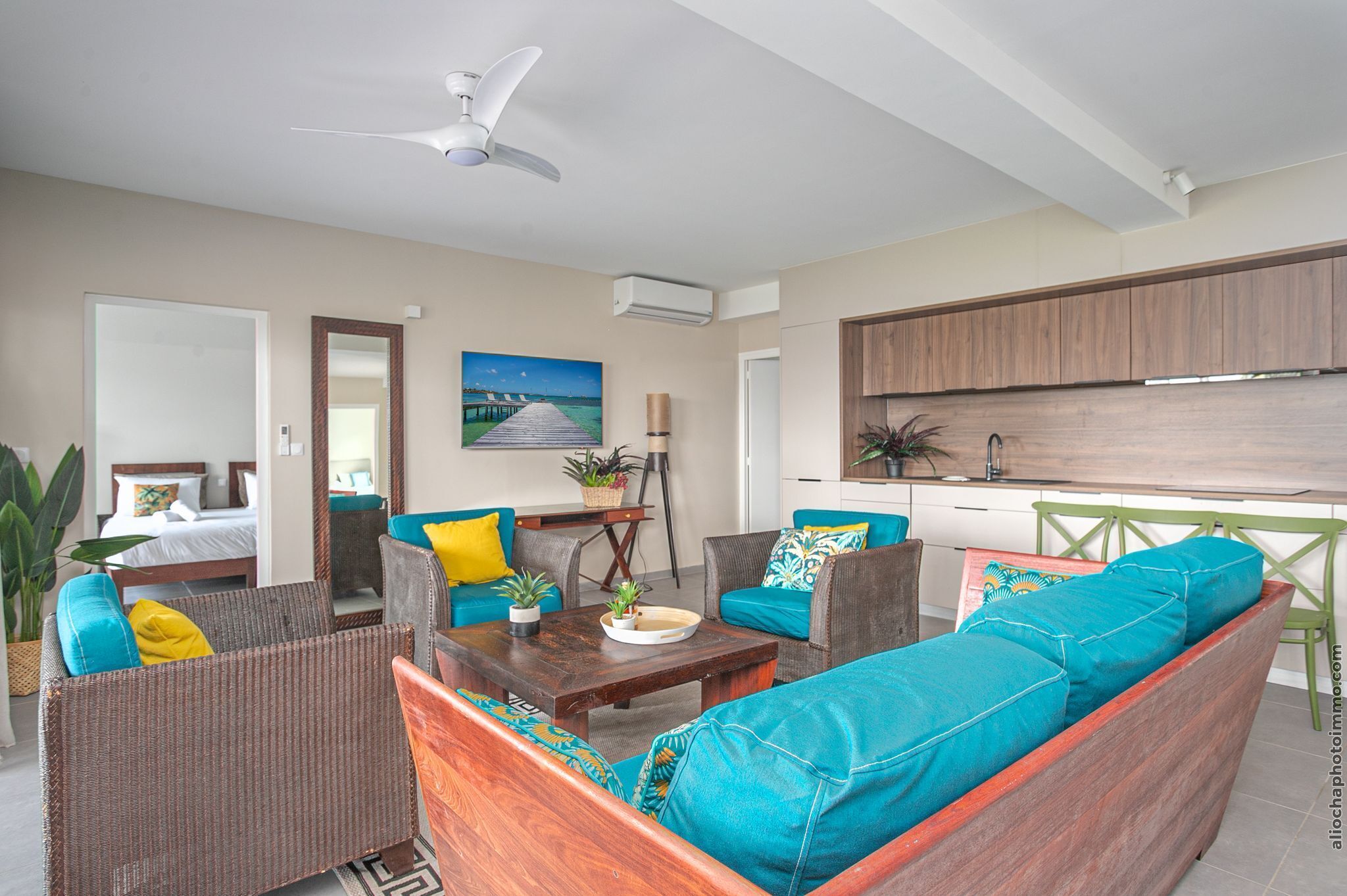A modern living room with a sofa, armchairs, a coffee table, and a dining area with a kitchen in the background.