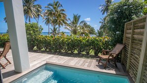 A pool area with wooden deck, lounge chairs, and a view of the ocean and palm trees. - VILLAS MAORIE (Le Francois)