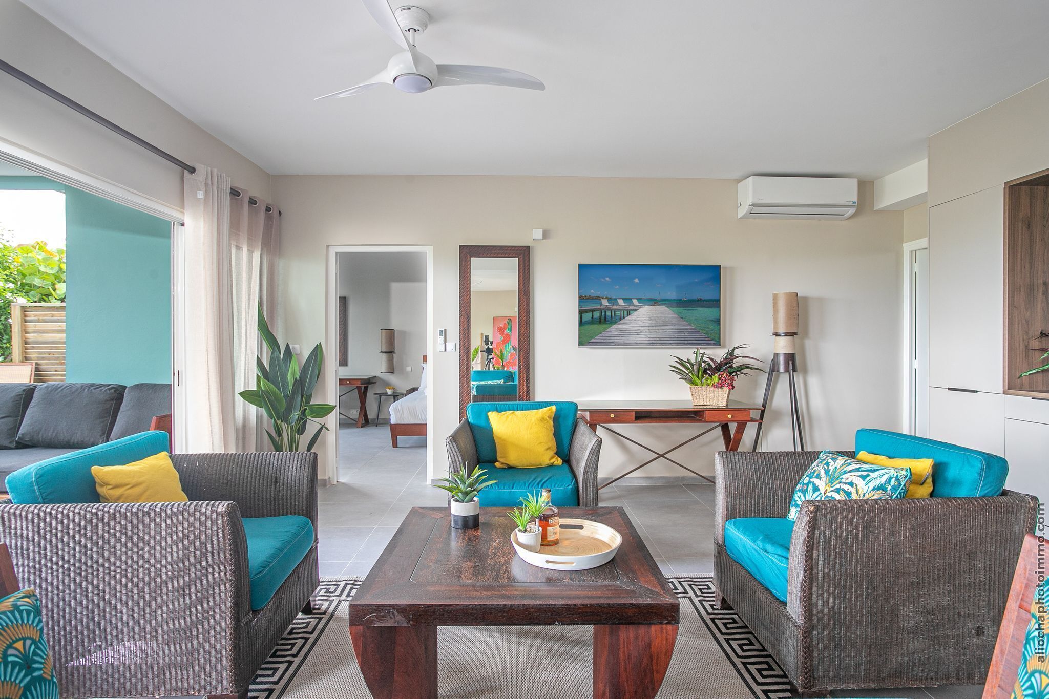 A modern living room with a ceiling fan, a dining area with a table and chairs, and a view of the outdoors through a sliding door.