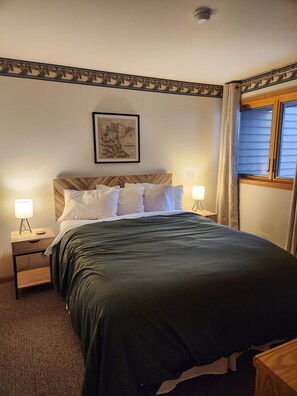 A bedroom with a bed, two bedside tables, a night lamp, a framed map on the wall, and a window with curtains. - Lake Superior Retreat Near Two Harbors; Waterfront Views + Access; Cozy getaway! (Two Harbors)