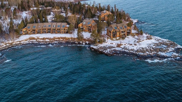 Eine Lodge mit mehreren Blockhütten auf einer verschneiten Insel, umgeben von Wasser und Bäumen.