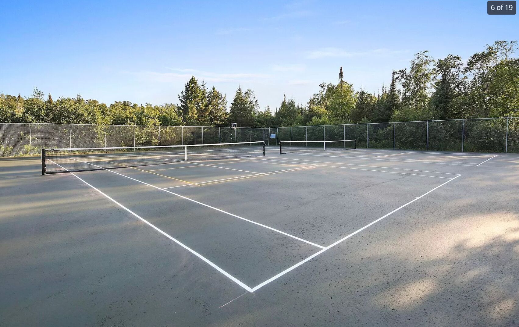 Un court de tennis en plein air, doté d’un filet et entouré d’arbres et d’une clôture.