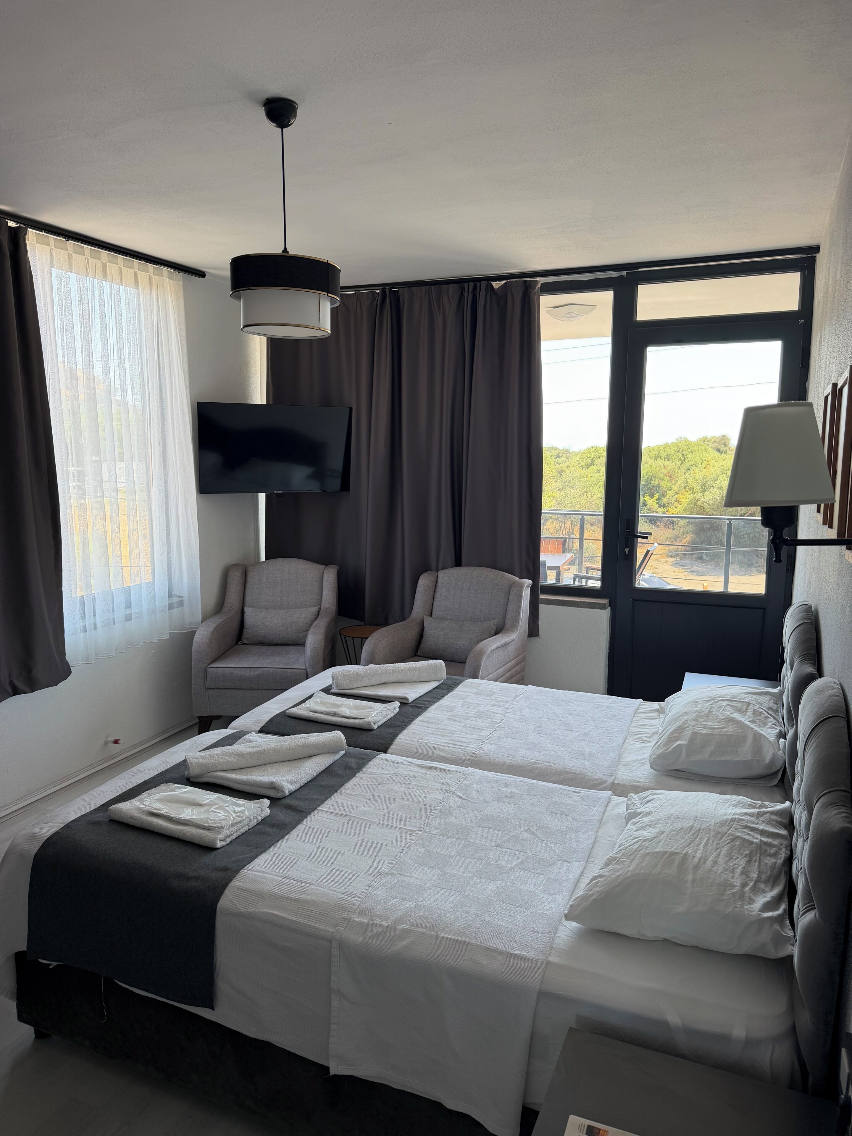 A hotel room with a bed, two armchairs, a TV, and a window with curtains.