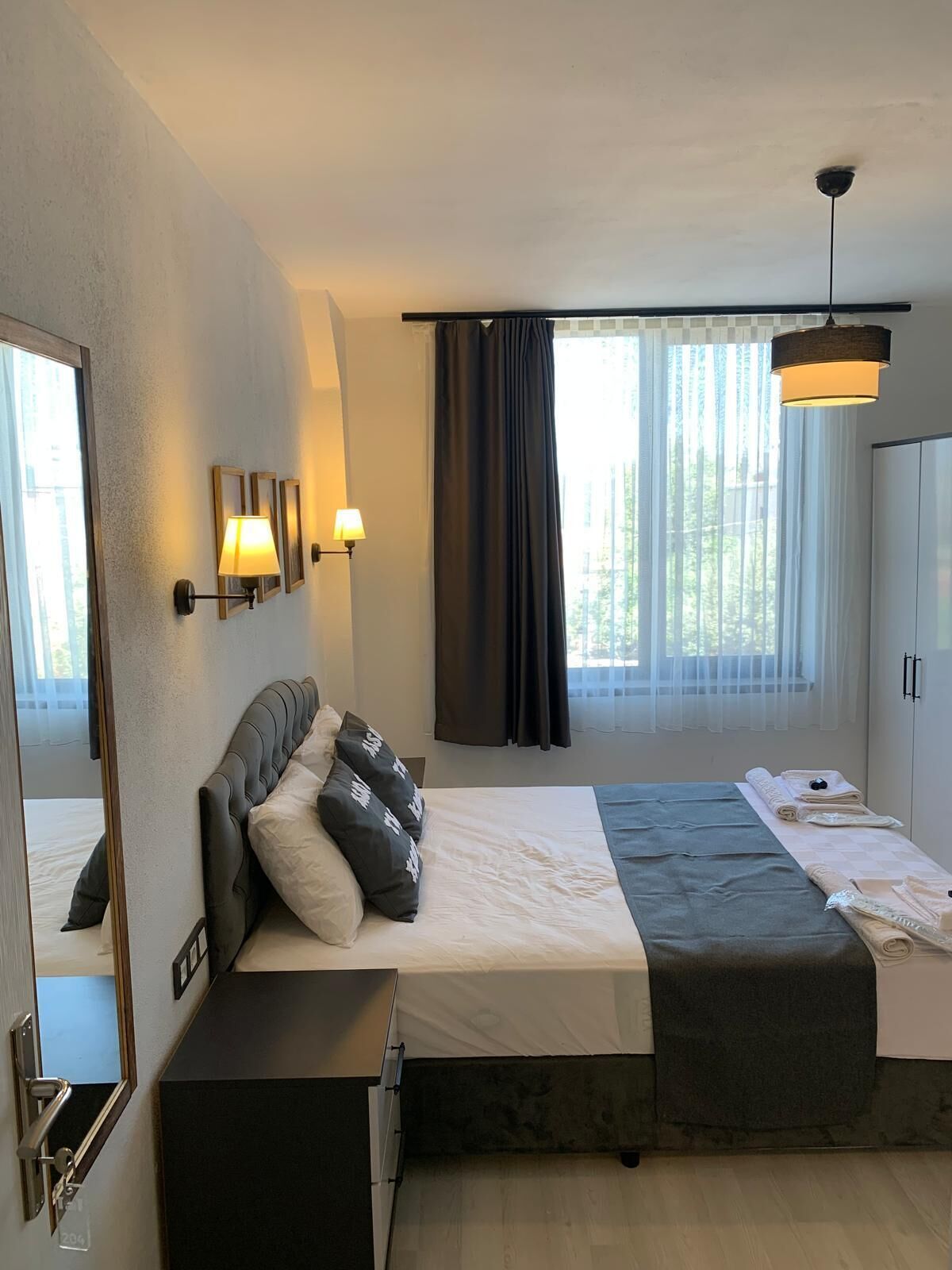 A modern bedroom with a large bed, a bedside table, a mirror, and a wardrobe.