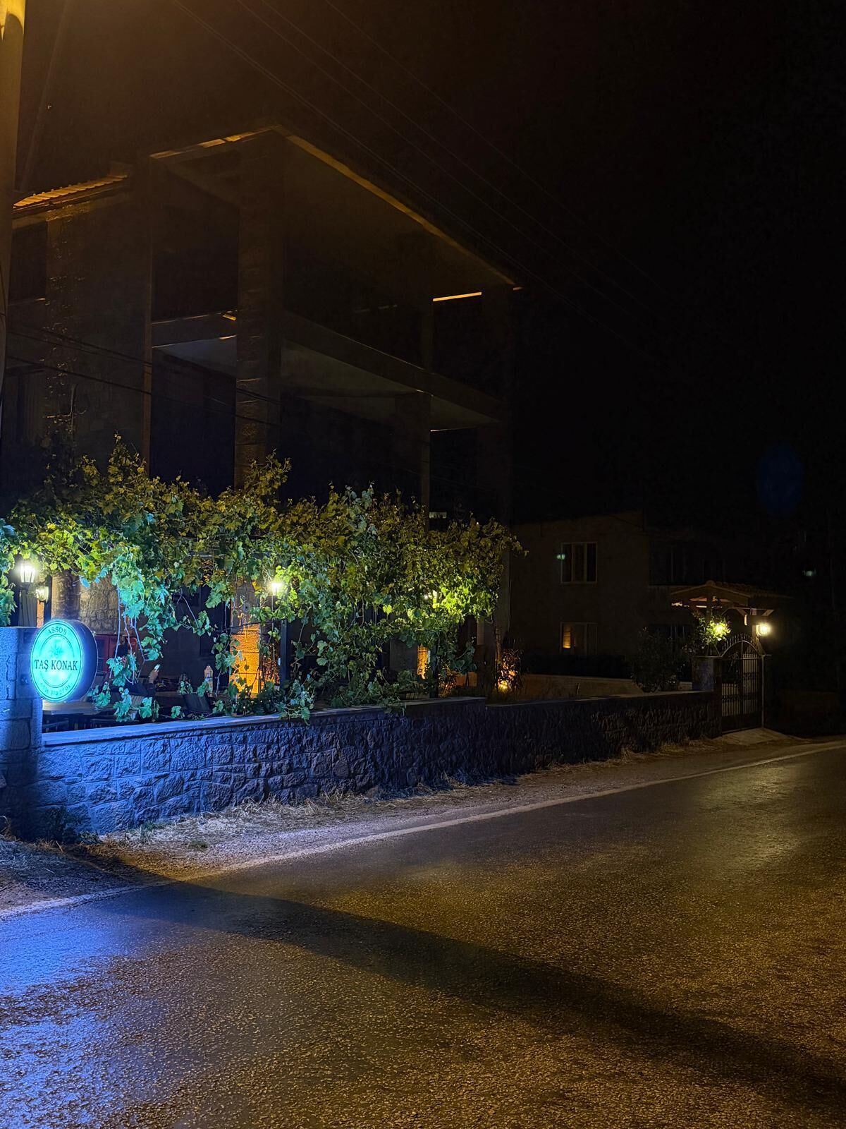 Vue nocturne d'un bâtiment doté d'un mur en pierre et d'une enseigne sur laquelle on peut lire : « ASSOV TAS KONAK ».