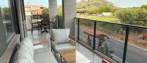 A balcony with a sofa, chairs, and a table, overlooking a road and greenery.
