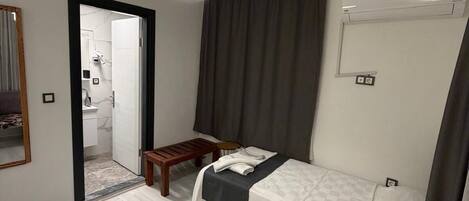 Een slaapkamer met een bed, een bureau, een stoel, een spiegel en een airconditioning.