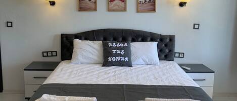 A neatly made bed with white linens, a dark headboard, and a pillow with text. There are wall-mounted lamps and framed artwork above the bed.