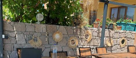 An outdoor patio with stone walls, wooden tables and chairs, and decorative sunshades.
