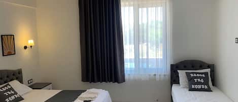 Habitación de hotel con dos camas, un ventanal con cortinas translúcidas, un aire acondicionado de pared y un aplique de techo.