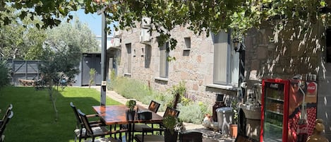 An outdoor patio with a wooden table and chairs, a stone building in the background, and a Coca-Cola vending machine.
